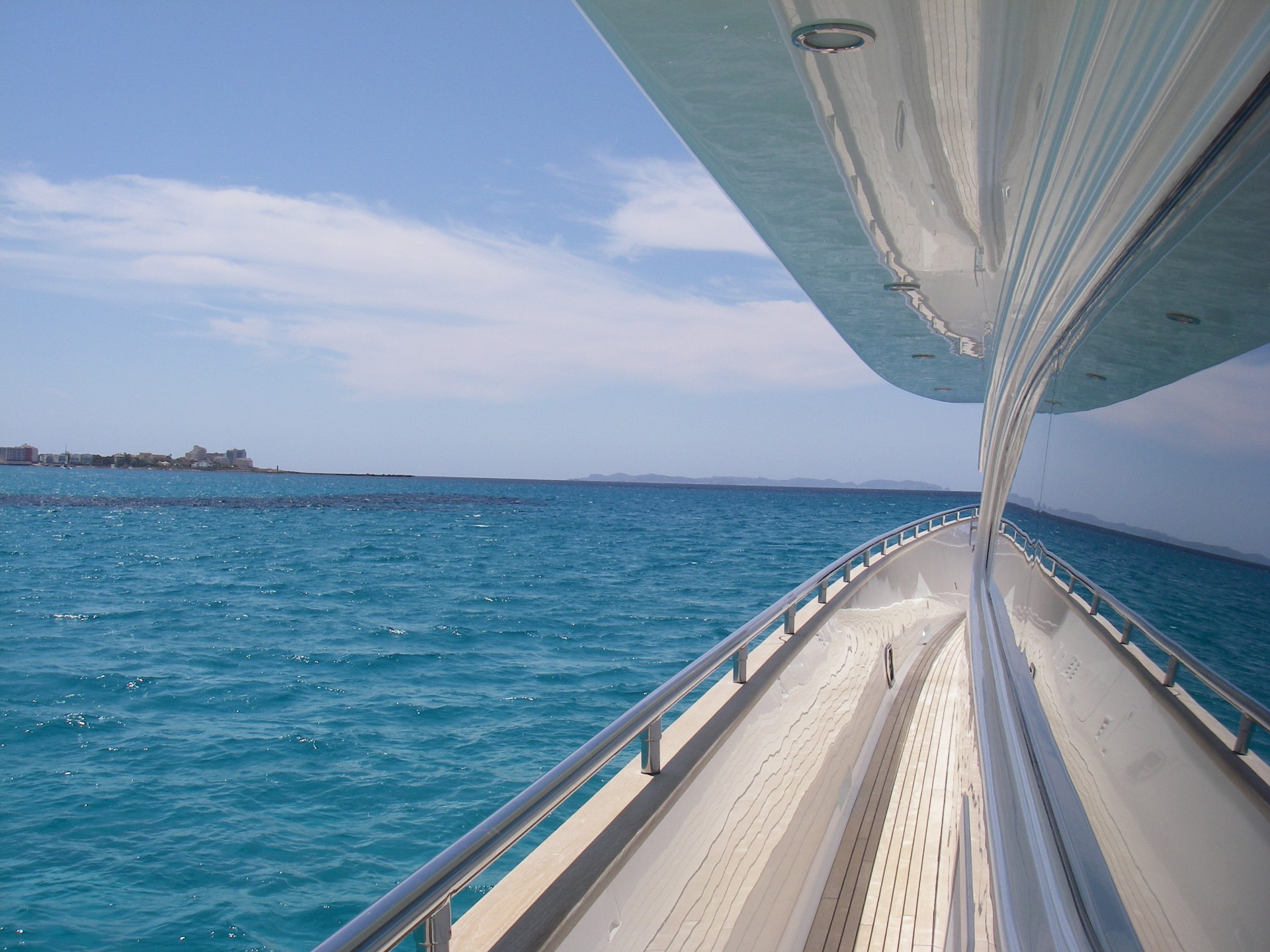 View from a superyacht bow over bright turquoise water with the yacht's deck and rail in the foreground