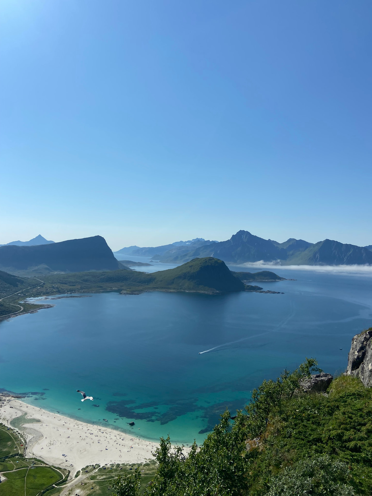 Turquoise bay and white sand beach surrounded by green mountains under a clear blue sky